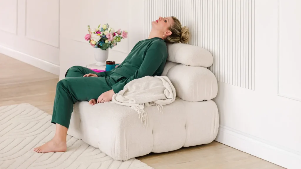 Libby Ward slouches on a sofa with a look of defeat on her face as she is experiencing overstimulation as a mom.